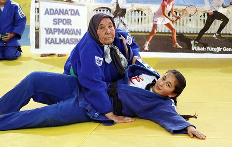old woman in blue gi on jiu jitsu mat with younger woman in blue gi