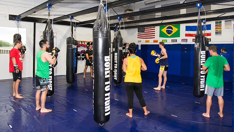 fort collins kickboxing students watching coach in a blue shirt demonstrate a technique on the heavy bag