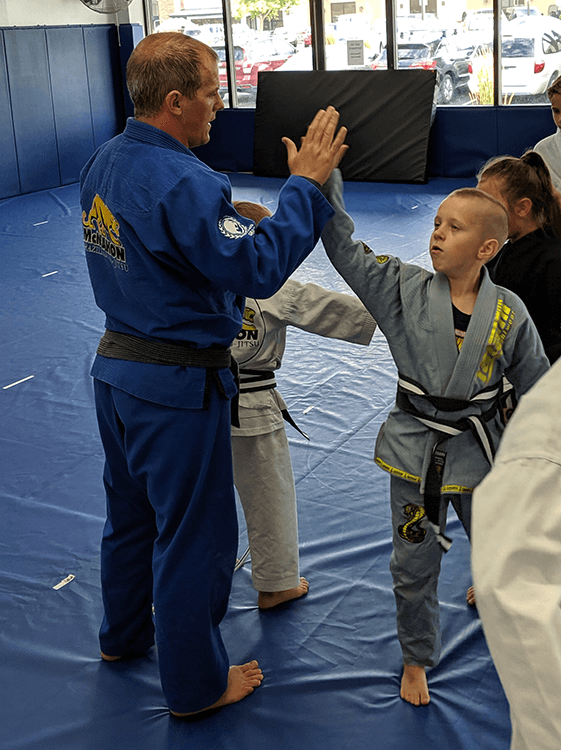 Finnie mcmahon in blue gi high fiving kids brazilian jiu jitsu student in grey uniform