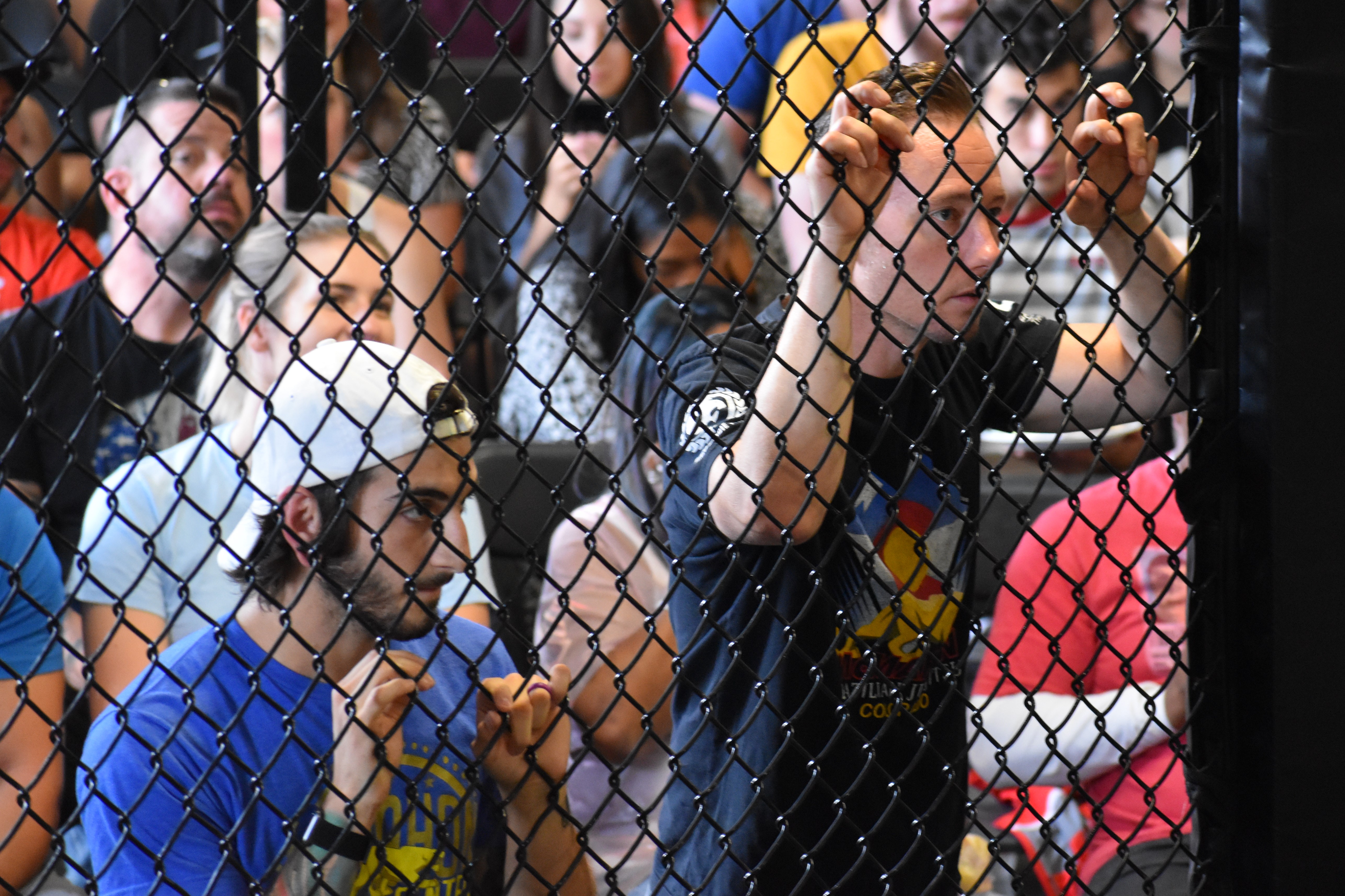 two muay thai coaches watching a fighter compete behind a MMA cage